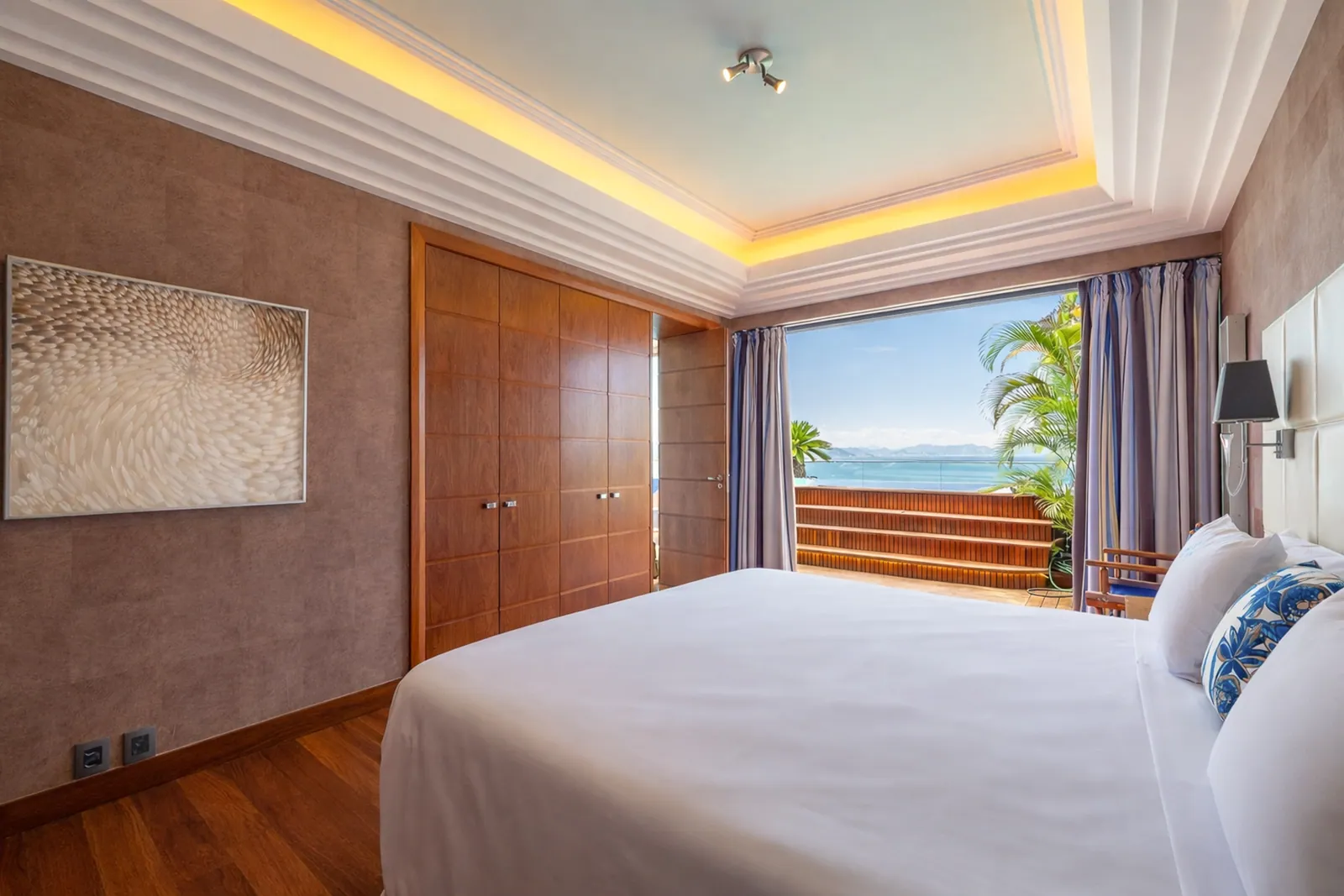Wood-panelled bedroom with padded headboard, terrace beyond the glass