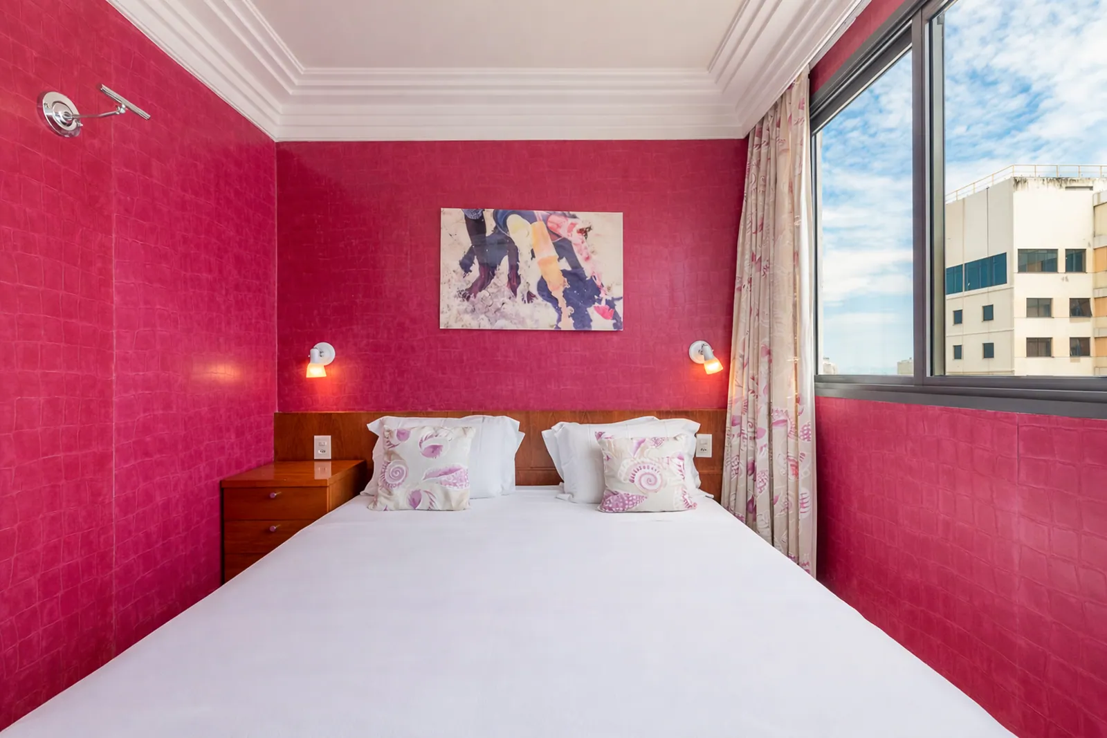 Bedroom with deep pink walls, window onto the rooftops