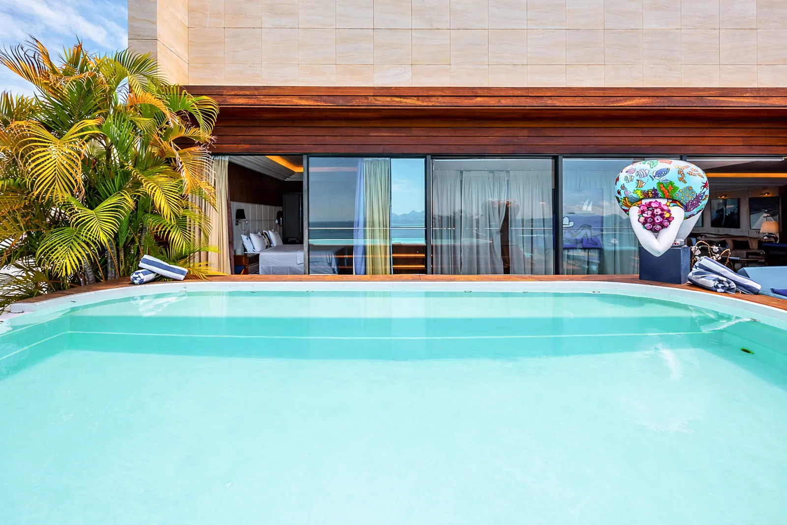 The pool framed by palms, bedroom doors opening onto the deck